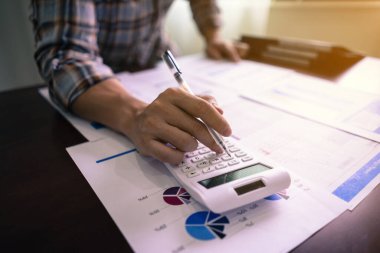 İş muhasebesi, iş adamı hesap makinesi kullanıyor ve ofiste bütçe ve kredi kağıtlarıyla istatistik raporu okuyor.
