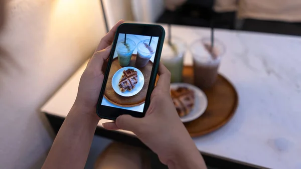 Üst Manzara. Kadın cep telefonuyla mini şekerli kek ve kahvenin fotoğrafını çekiyor. Cep telefonlu fotoğraf ve tatil seyahati konseptinde rahatlama.