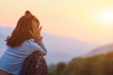 Kadın bir sandalyeye oturdu ve sabah uyandıktan sonra altın güneş ışığının bulanık arka planına uzandı. Genç bir turist, villadan çıktıktan sonra rahatlamak için tembelce geriniyor..