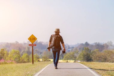 Bulanık görüntü, uzun kollu elbise giymiş genç bir fotoğrafçı ve kamera çantasıyla turizm tanıtımı için fotoğraf ve video kayıt yerlerini keşfetmek üzere yolda yürüyor..