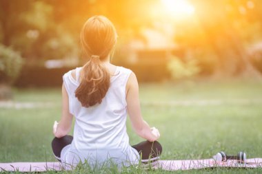Kız, meditasyon yapmak ve Tanrı 'dan dua etmek için parkta çimlerin üzerinde bir mindere oturur. Vücudunu sağlıklı tutmak için ve meditasyon duruşu da yoganın başka bir şekli, Tanrı 'ya inanın.