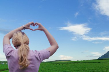 Kız anlamlı bir kalp sembolü göstermek için elini kaldırıyor. Ona seni doğanın bulanık arka planında sevdiğimi söyle. Sevgililer Günü 'nde aşkı anlatan semboller gösterme konsepti