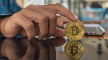 Genç bir işadamı Bitcoin 'i elinde tutuyor çünkü sanal paraya ya da kripto para birimlerine yatırım yapmaya inanıyor. Şifreleme parasının sembolü olan bir altın sikke.