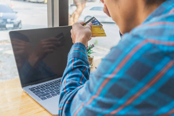 A young man with a credit card in his hand, sitting in agitation in front of a computer when he sees a debt collection document from the credit card company for unable to pay the credit card debt.