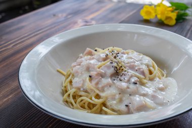 spagetti carbonara, lezzetli bir jambon, pastırma ve sıcak peynir karışımı, ahşap bir masada beyaz bir tabakta servis edilir. Jambon, pastırma ve peynirle karıştırılmış Carbonara soslu lezzetli spagetti..
