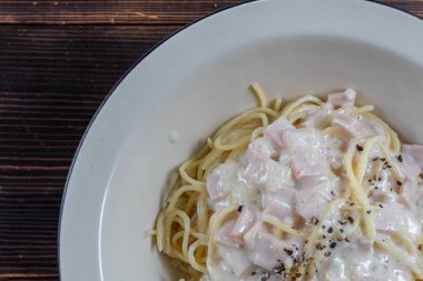 spagetti carbonara, lezzetli bir jambon, pastırma ve sıcak peynir karışımı, ahşap bir masada beyaz bir tabakta servis edilir. Jambon, pastırma ve peynirle karıştırılmış Carbonara soslu lezzetli spagetti..