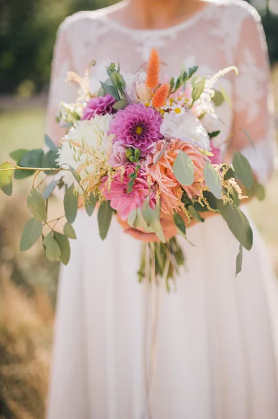 Noiva em um vestido branco segurando um buquê de peônias brancas e flores de rosa e vegetação no fundo da grama — Fotografia de Stock