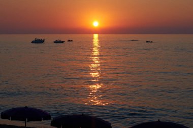 Güneşin son ışıklarının tadını çıkaran açık şemsiyeler ve tatilcilerle denizin üzerinde gün batımı