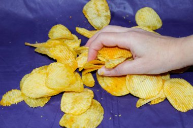 Bir kadının eli, üzerinde koyu mavi bir masa örtüsü olan bir masanın üzerindeki cipsleri topluyor. Kapat.