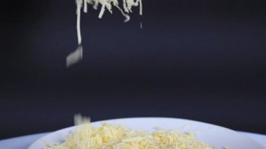 Sert rendelenmiş peynir tabağın üzerine siyah arka planda serpiştirilir. yakın çekim, seçici odak.