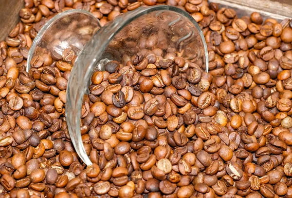Roasted coffee beans are scattered on the surface and poured into a glass vase that stands in the middle. Selective shot, top view.