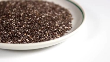 Chia tohumları beyaz arka planda bir fincan tabağının üzerine serpiştirilir. Seçici odak.