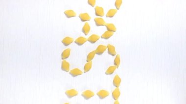 Makarna kelimesi beyaz dönen bir masada çiğ makarnanın üzerine serilmiştir. Yukarıdan görünüşü.