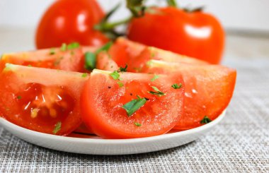 Put the sliced red tomato on a plate, sprinkle with spices and green onions. blurry, Close-up, selective shot.