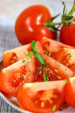 Place the sliced red tomato on a plate, sprinkle with spices and green onions. Blurry, vertical frame, selective shot.