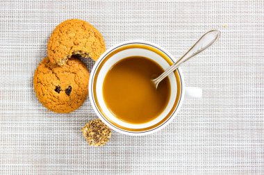 Kahve ve süt bardakta, kemirilmiş yulaflı kurabiye ve yanında da bir çikolata. Üst görünüm.