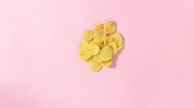 Hareket animasyonunu durdur. Kuru mısır gevreği pembe arka planda hareket eder. Süper yemek. Üst görünüm.
