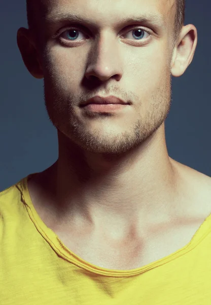 Joven hombre guapo y de ojos azules con mirada pensativa en camiseta de color amarillo brillante posando sobre fondo gris. De cerca. Captura de estudio — Foto de Stock