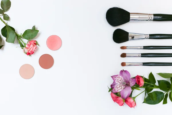 Makyaj kozmetik, fırçalar, shadoes ve beyaz arka plan üzerinde çiçekler ile kompozisyon