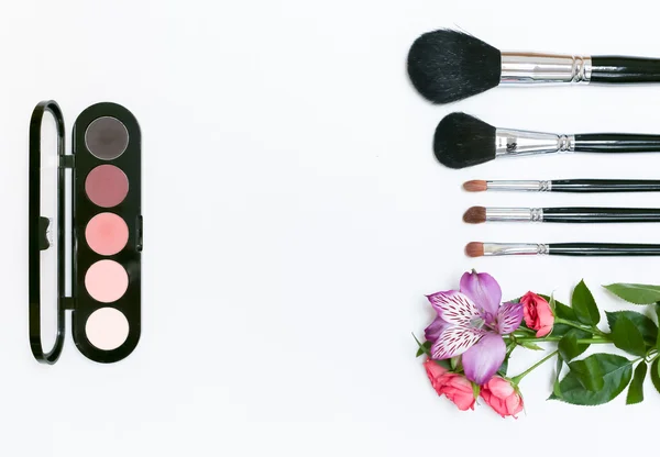 Makyaj kozmetik, fırçalar, shadoes ve beyaz arka plan üzerinde çiçekler ile kompozisyon