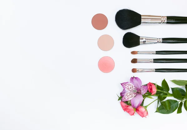 Makyaj kozmetik, fırçalar, shadoes ve beyaz arka plan üzerinde çiçekler ile kompozisyon