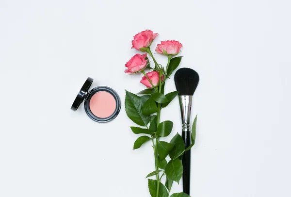 Komposition mit Make-up-Kosmetik, Pinseln, Schatten und Blumen auf weißem Hintergrund Stockbild
