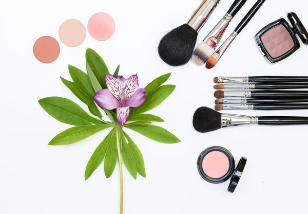 Composición con cosméticos de maquillaje, pinceles, sombras y flores sobre fondo blanco Imagen De Stock