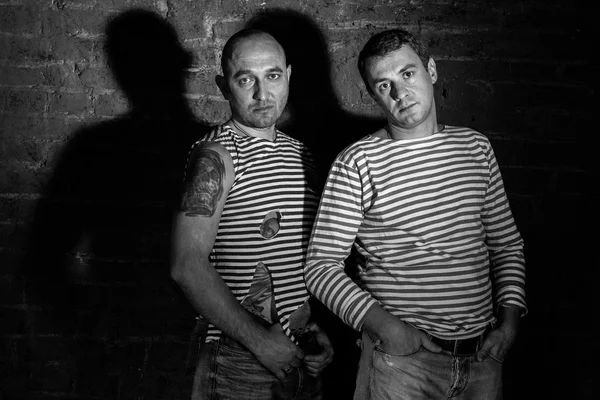 Siyah-beyaz tarzda tuğla duvara yakın duran iki adam