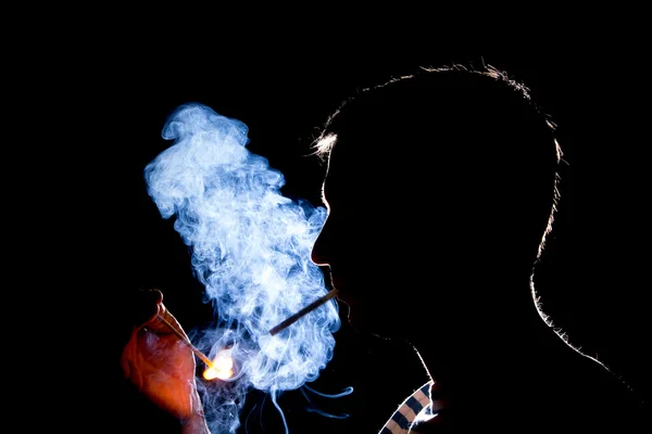 Silueta del hombre que enciende el cigarrillo en la oscuridad Imagen De Stock