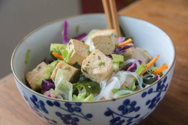 İçinde tofu, kırmızı lahana, marul, Wakame deniz yosunu ve havuç bulunan Vietnam eriştesi salatası. Bir kasede servis edildi..
