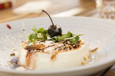 Türkiye kökenli geleneksel bir süt pudingi olan Muhallebi, süt ve mısır çiçeğinden yapılmış, badem, şeker tozu ve kirazla birlikte beyaz bir tabakta servis ediliyor.