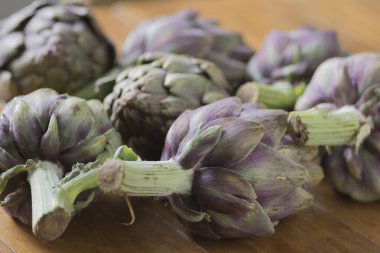 Güzel Globe Enginarları (Cynara cardunculus var. Aynı zamanda yeşil ve mor renklerde Fransız enginarı ve yeşil enginar olarak da bilinir, ahşap bir masanın üzerine yığılmıştır.