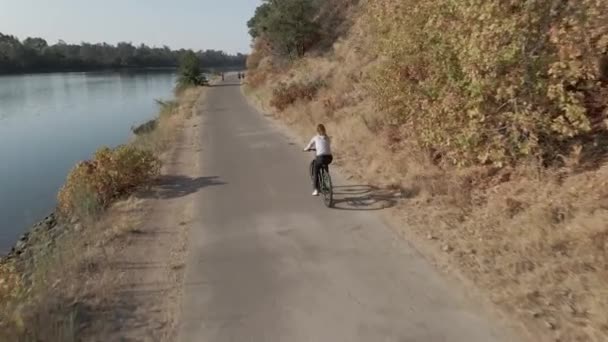 4K Den vackra damen rider på cykeln längs en flod — Stockvideo