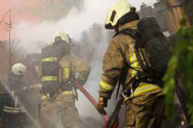 Kasklı ve koruyucu teçhizatlı iki itfaiyecinin duman ve püskürtücü suyla çevrili bir yapı yangınıyla mücadele edişini izleyin. Yüksek kalite fotoğraf