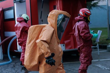 Kırmızı ve turuncu kimyasal korumalı tehlikeli madde giysileri ve yüz maskeleri giymiş acil durum ekipleri dezenfekte ya da kaza bölgesinde kırmızı müdahale aracının yanında bekliyorlar. Yüksek kalite fotoğraf