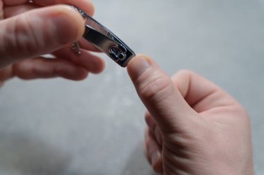 Close-up of a person carefully trimming fingernails using a metal nail clipper at home, highlighting personal grooming and hygiene on a neutral background. High quality photo