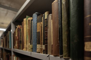 A row of old, worn books with faded and tattered covers, lined up closely on a library or archive shelf in a dimly lit room. High quality photo