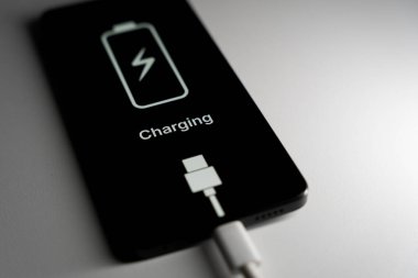 Akıllı telefon ekranında şarj edilmiş bir pil simgesi ve siyah arkaplanda şarj kelimesi görülüyor. Yüksek kalite fotoğraf