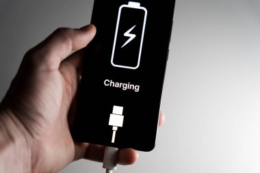 Elinde akıllı bir telefon olan ve siyah ekranda şarj edilmiş bir pil ve metni gösteren bir el. Yüksek kalite fotoğraf