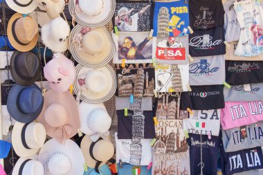 İtalya 'nın Pisa kentindeki hediyelik eşya dükkanında Eğik Kule ve İtalya temalı baskıların yer aldığı tişörtler ve şapkalar. 2025, 12 Haziran