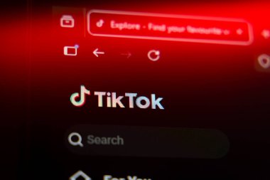 Viral sosyal medya eğilimleri ve dijital eğlenceyi temsil eden canlı kırmızı ışık altında resmi logo ve arama çubuğunun yer aldığı akıllı telefon ekranındaki TikTok mobil uygulaması veya web sitesi arayüzü. Yüksek kalite fotoğraf
