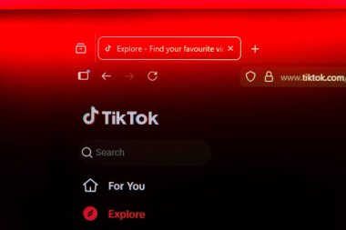 Viral sosyal medya eğilimleri ve dijital eğlenceyi temsil eden canlı kırmızı ışık altında resmi logo ve arama çubuğunun yer aldığı akıllı telefon ekranındaki TikTok mobil uygulaması veya web sitesi arayüzü. Yüksek kalite fotoğraf