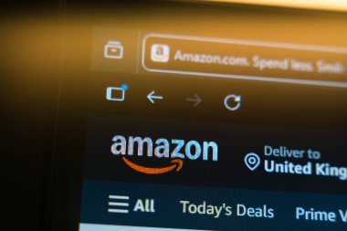 Amazon anasayfası, resmi logo ve tarayıcı sekmesinin bulunduğu bir bilgisayar ekranında küresel e-ticaret, çevrimiçi alışveriş ve dijital perakende pazarını temsil eden sıcak bir altın ışıkta sergilenmektedir. Yüksek kalite fotoğraf