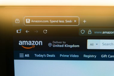 Amazon anasayfası, resmi logo ve tarayıcı sekmesinin bulunduğu bir bilgisayar ekranında küresel e-ticaret, çevrimiçi alışveriş ve dijital perakende pazarını temsil eden sıcak bir altın ışıkta sergilenmektedir. Yüksek kalite fotoğraf