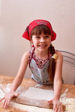 Küçük mutlu şef, un, hamur yoğur. Kız aşçı hamuru merdaneyle yuvarlıyor. Ev yemeği. Mutfak
