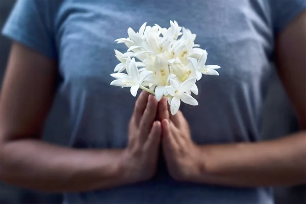 Mulher orando com flores brancas nas mãos sobre fundo escuro — Fotografia de Stock