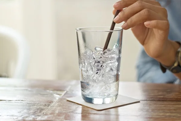 Vaso de agua y hielo en la mano sobre la mesa de fondo del restaurante — Foto de Stock
