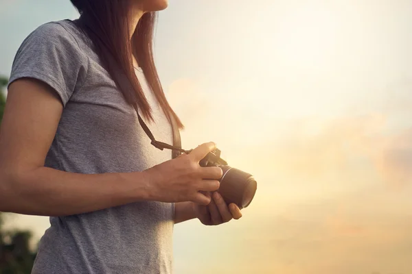 Mulher segurando câmera na mão no pôr do sol natureza fundo — Fotografia de Stock