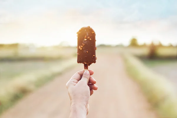 Mão de mulher segurando um picolé de chocolate no fundo da natureza — Fotografia de Stock