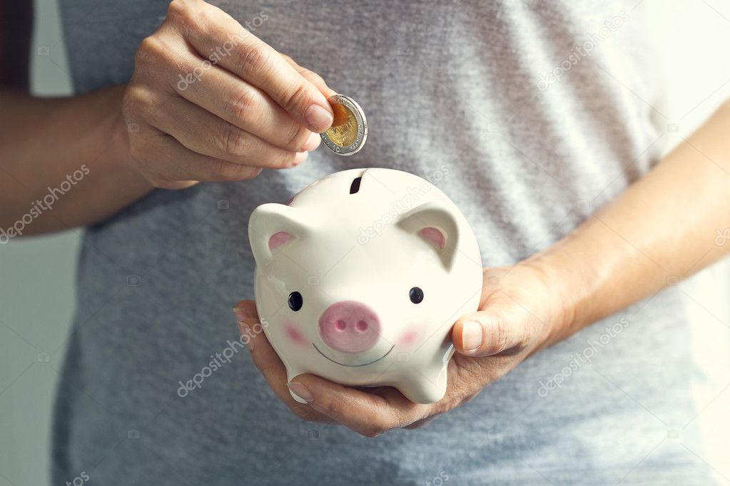 Woman hand putting coin into piggy bank 